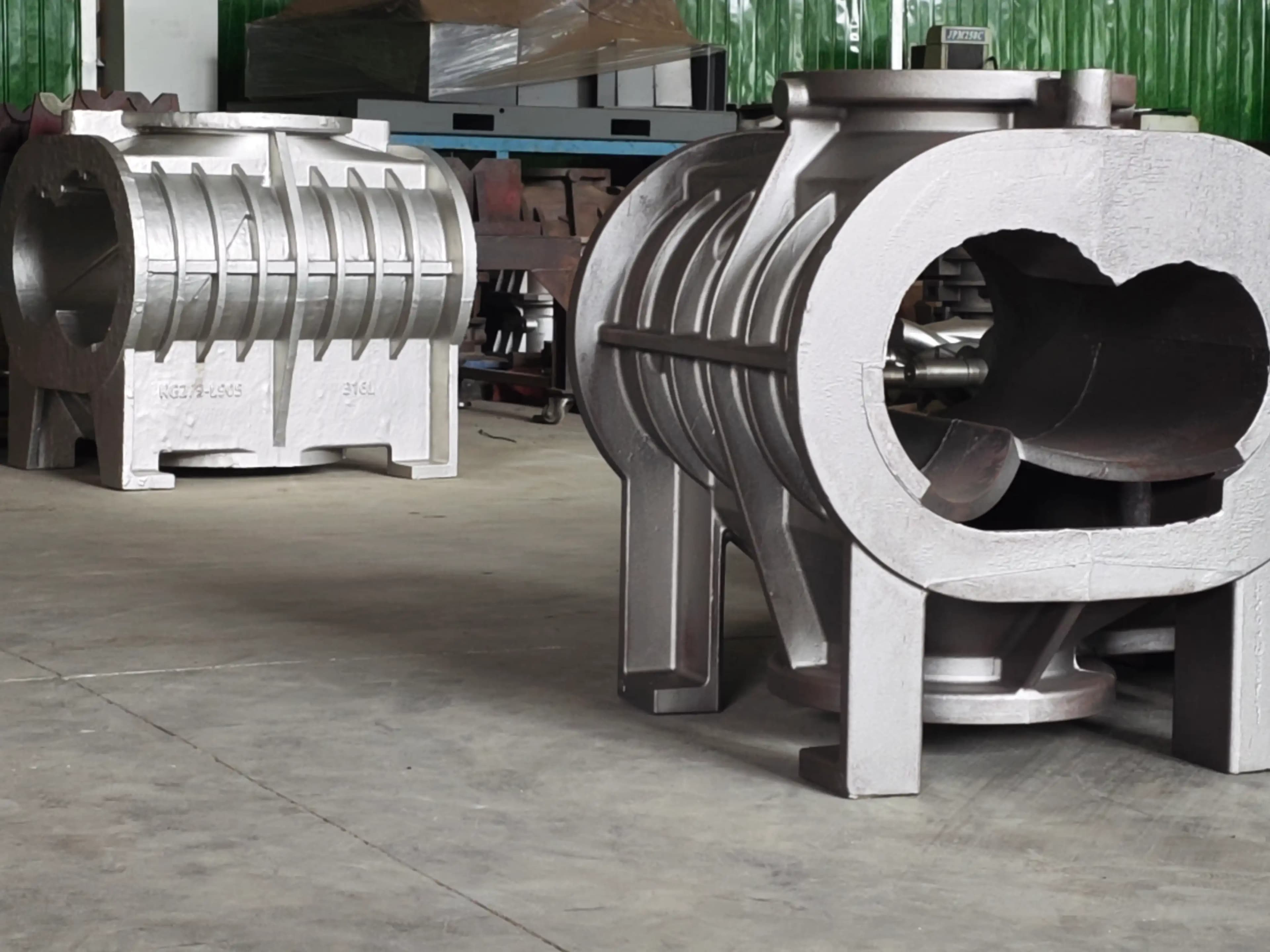 316 stainless and ASTM A48 Class 35 dry screw vacuum pump housings on a shop floor, shown side by side for material comparison