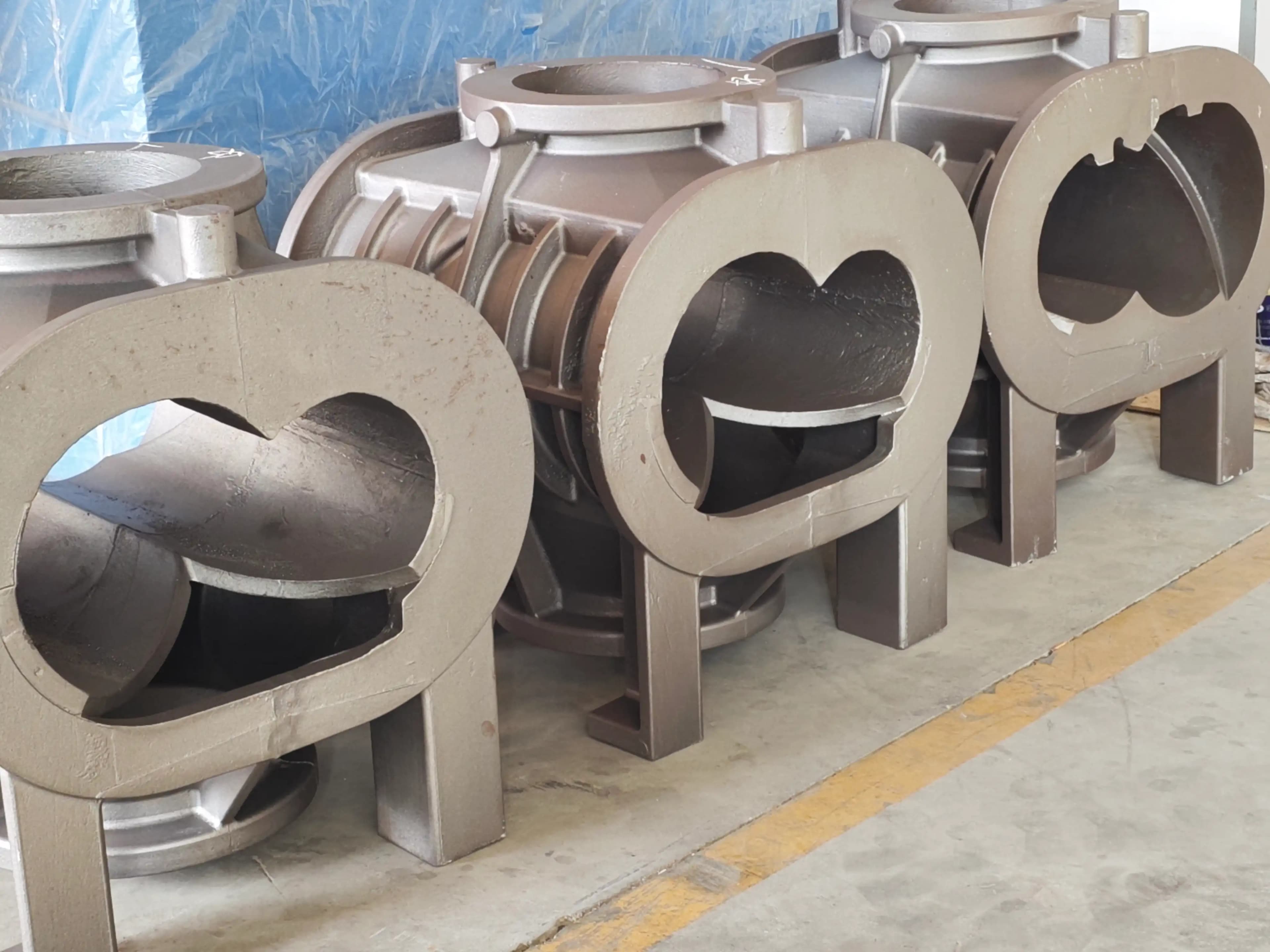 Cast dry screw vacuum pump casings lined up on the shop floor before bore finishing, showing the characteristic twin-bore figure-eight profile through the end face
