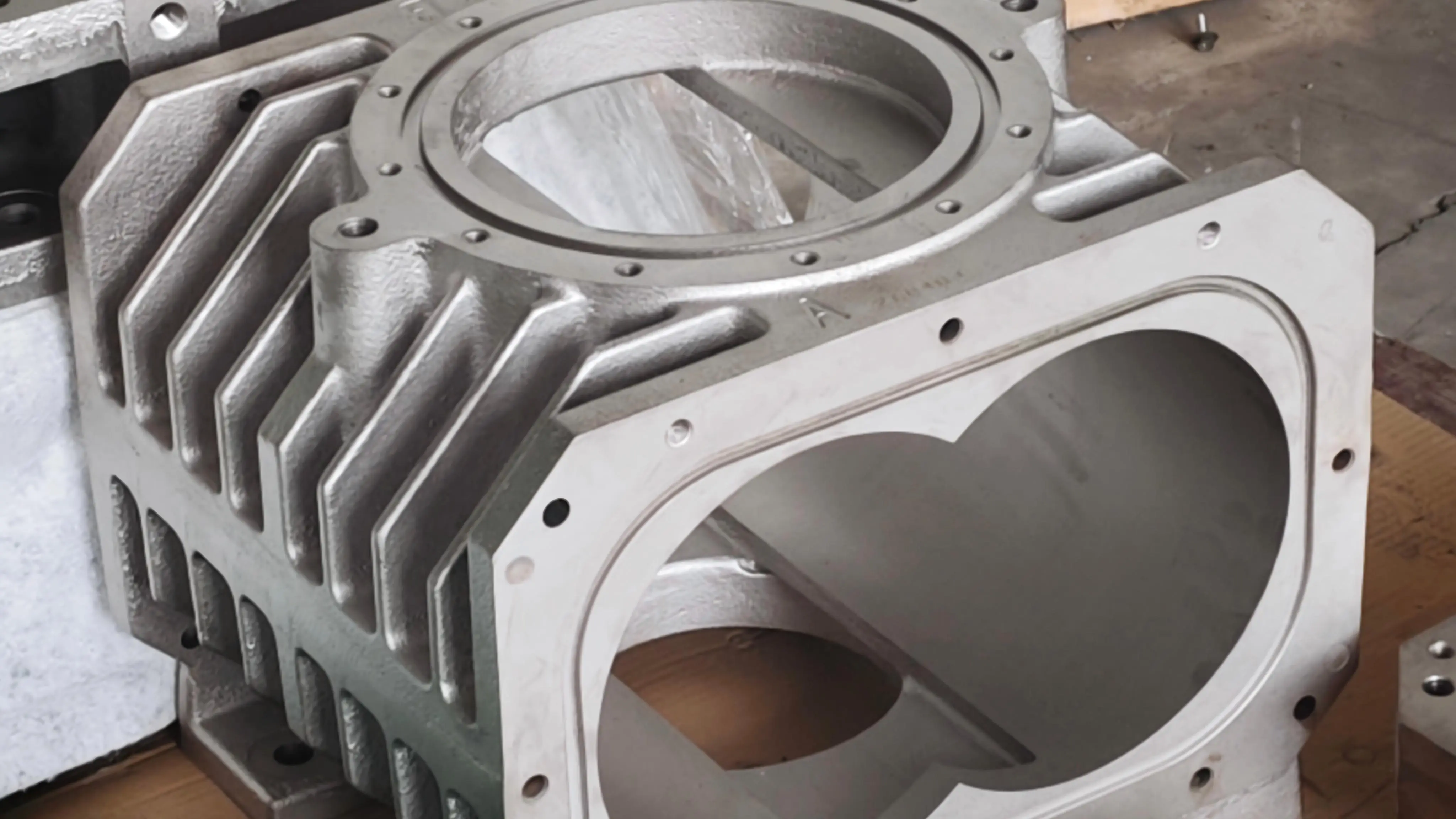Hastelloy-coated dry screw vacuum pump housing showing the twin-bore figure-eight profile on the end face, integral cooling fins, and mounting-flange bolt circle — returned from SCPM's qualified finishing-partner network for final inspection.