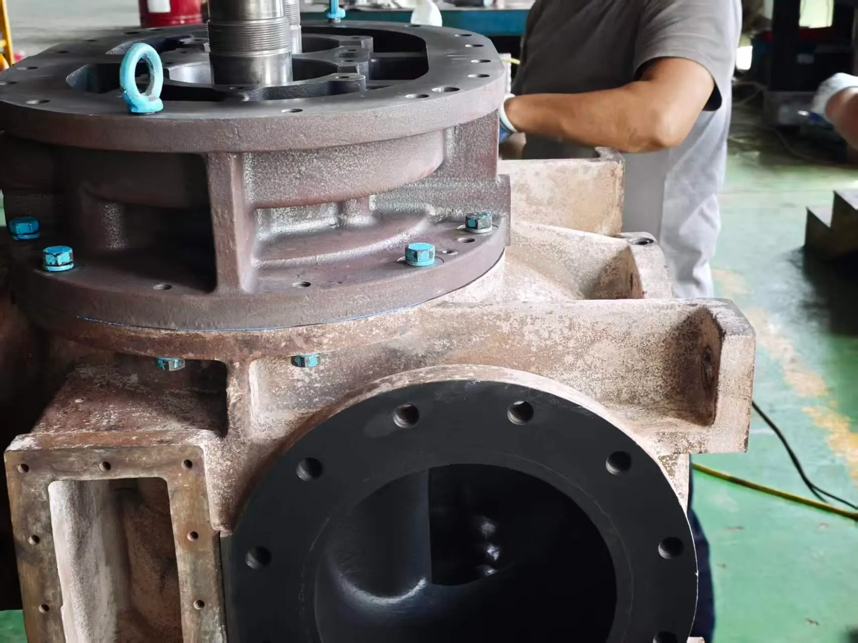 Cast dry screw vacuum pump housing during assembly on the shop floor, with the rotor shaft installed through the top end cover and the discharge flange visible below