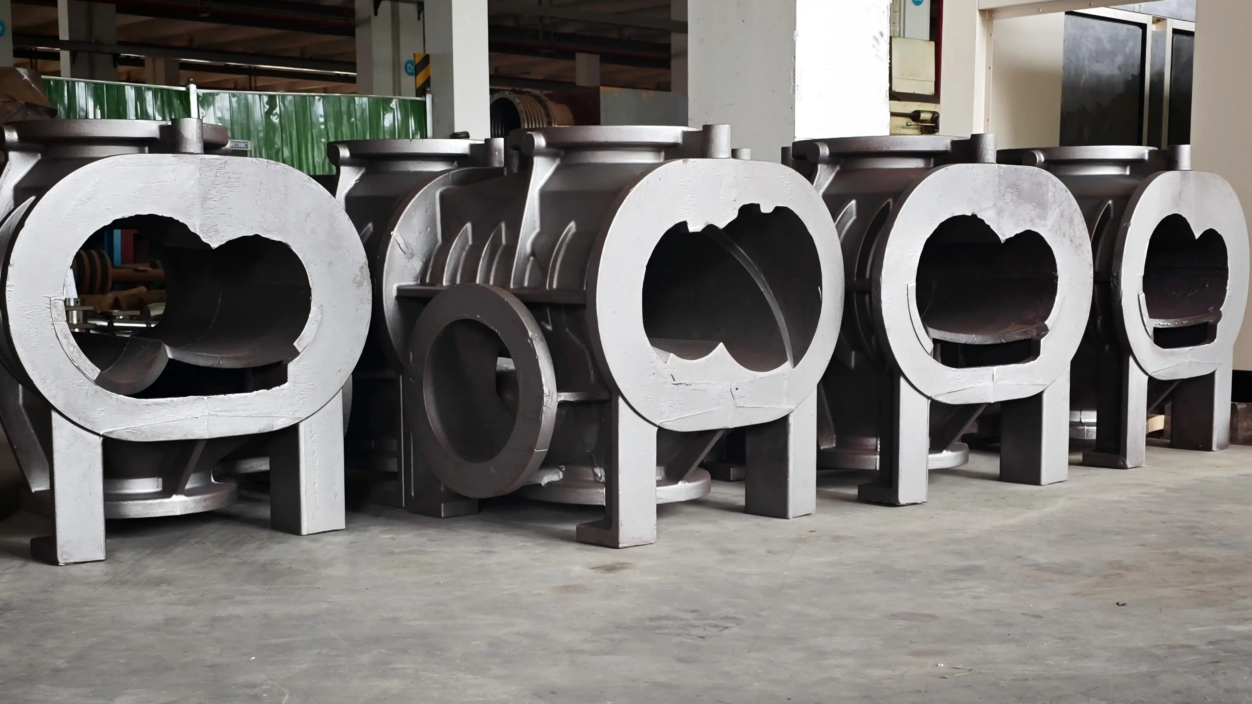 Row of dry screw vacuum pump housing castings on a shop floor, showing the twin-bore openings and ribbed outer walls before final machining