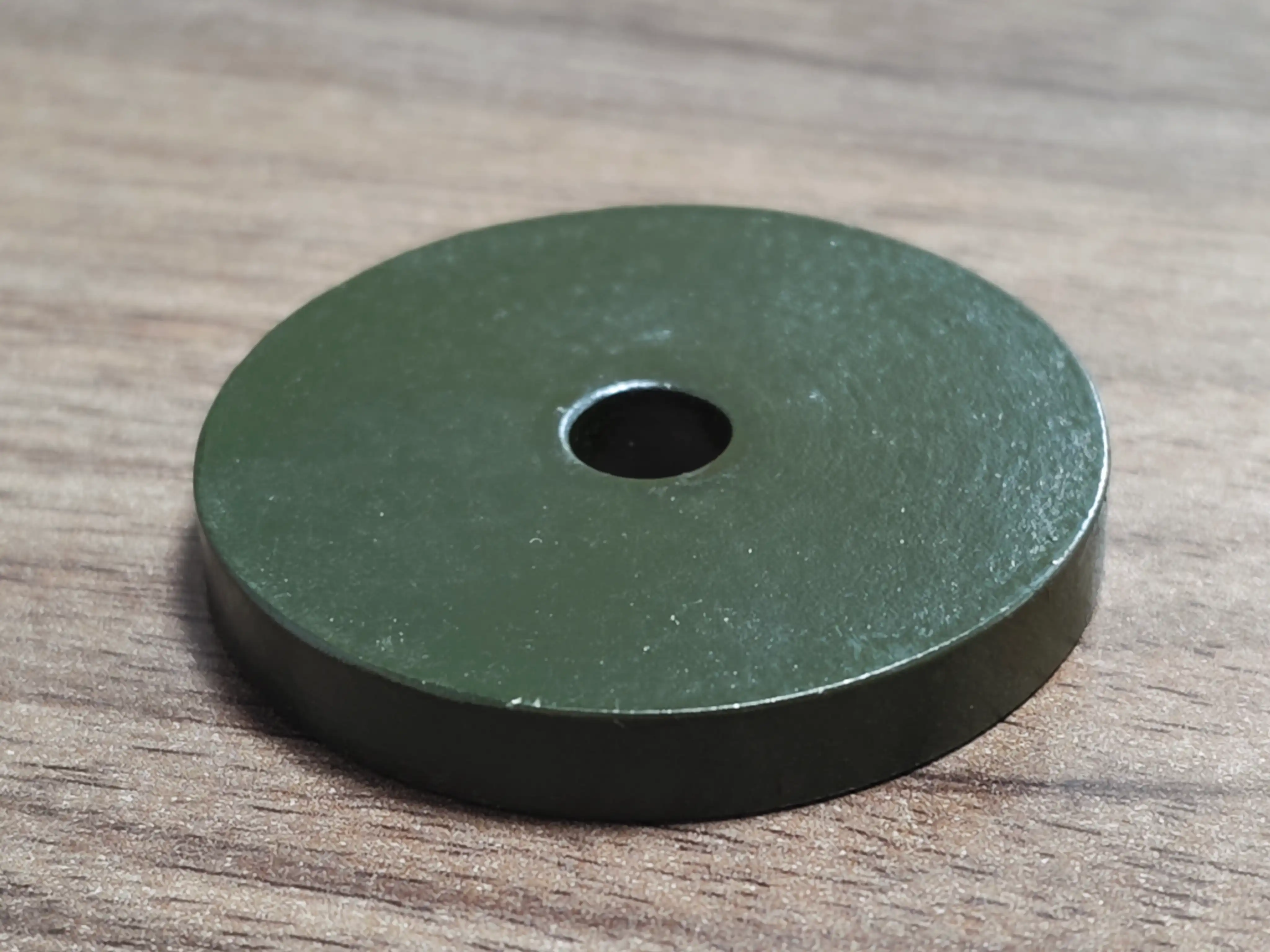 Green coated round Class 35 test coupon with a center hole, used for corrosion validation before changing a dry screw pump housing material